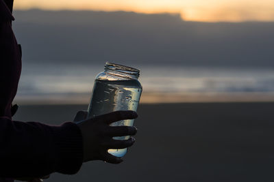 Cropped hands holding water in jar at beach