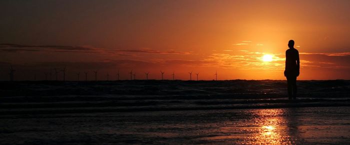 Silhouette iron man sculpture on crosby beach against sunset sky