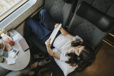 Directly above shot of girl using tablet pc while lying on seat in train