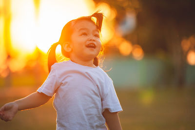 Girl looking away while standing on grass at sunset