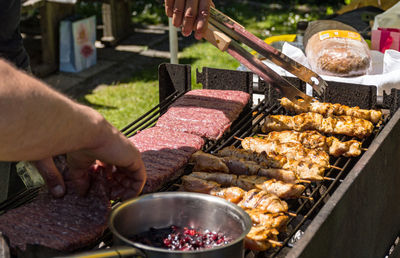 Close-up of man holding utensil and grilling meat in back yard.