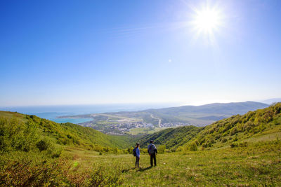 High angle view of couple standing on green mountain during sunny day