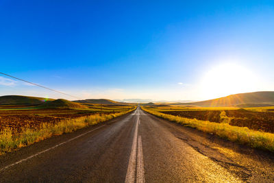 Empty road amidst field against sky