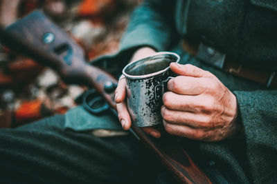 Midsection of soldier holding metal cup and gun