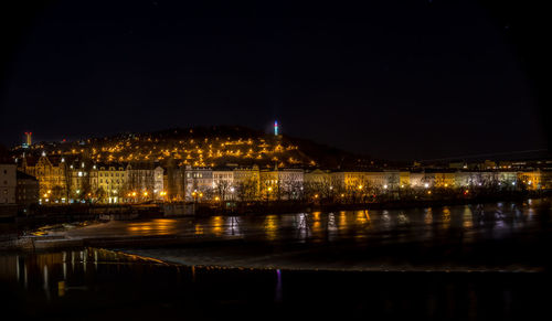 Illuminated buildings by river against sky at night