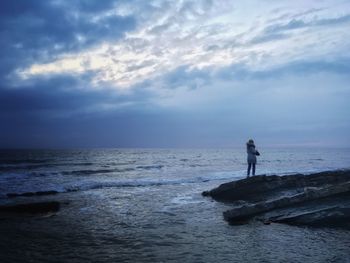 Man standing on rock at beach against sky