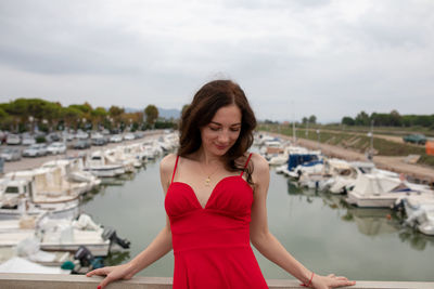 Woman wearing red dress while standing against boats moored at harbor