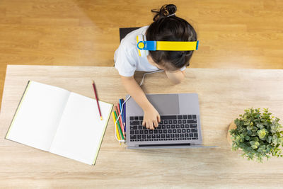 Top view shot of adorable asian girl kid, wearing headphone and typing keyboard, is learning online 