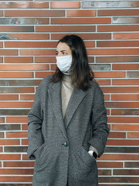 Portrait of young woman standing against brick wall