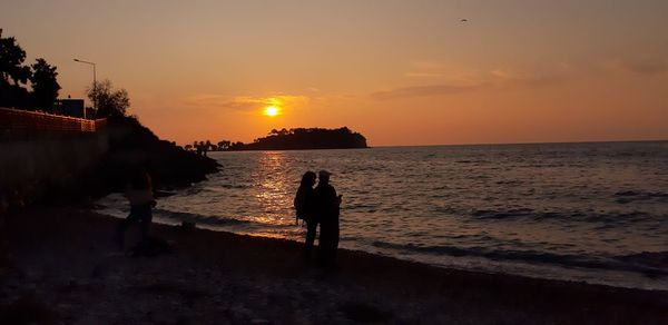 Silhouette people standing on beach against sky during sunset