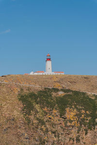 Lighthouse by mountain against clear blue sky