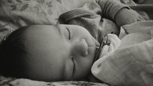 Close-up of baby boy with pacifier in mouth sleeping on bed