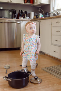 Portrait of cute girl standing on floor by utensils in kitchen at home