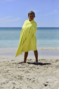 A boy stands on the seashore wrapped in a yellow towel. holidays. recreation. free space for text.