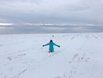 Rear view of person kneeling with dog on snow covered field against cloudy sky