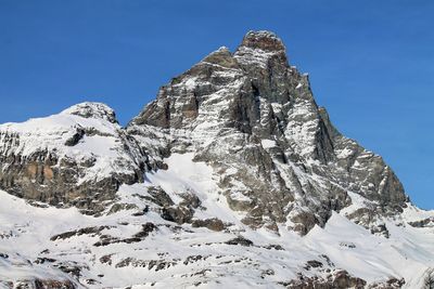 Low angle view of snowcapped mountain against clear blue sky