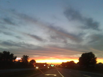 Road by silhouette trees against sky during sunset