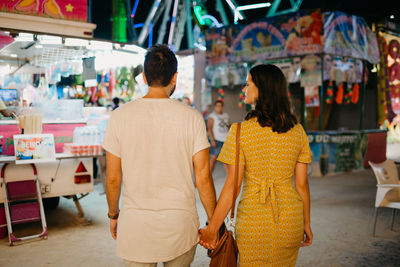 Rear view of couple holding hands at amusement park