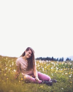 Young woman sitting on field against clear sky