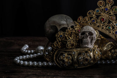 Close-up of human skulls and gold jewelry on table against black background