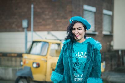 Portrait of smiling young woman standing against building in city