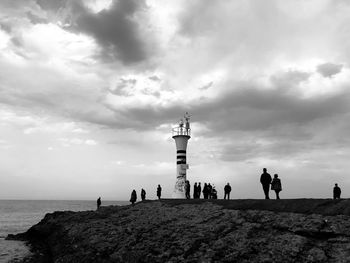 Silhouette people on beach by lighthouse against sky