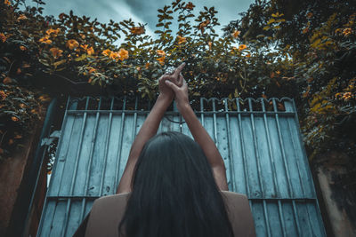 Rear view of woman relaxing while sitting on chair against gate