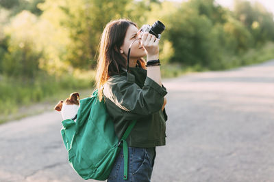 A charming young girl walks in nature, holding a backpack on her shoulder, from which her dog 