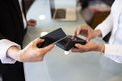 Female receptionist holding credit card reader while customer making contactless payment at hotel reception