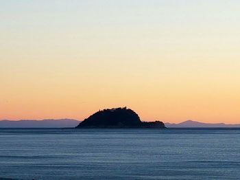 Silhouette rock by sea against sky during sunset