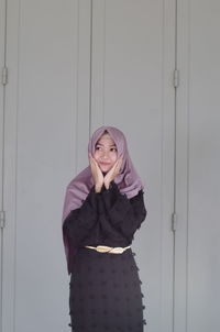 Portrait of smiling young woman standing against door