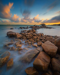 Rocks at sea shore against sky during sunset