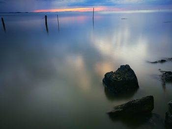 Rocks in sea against sky during sunset
