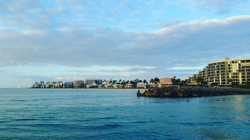 Scenic view of sea by buildings against cloudy sky