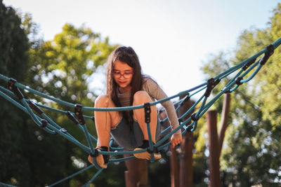 Caucasian girl sitting climbs on a rope swing in the park at the playground