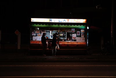 People walking on illuminated street in city at night