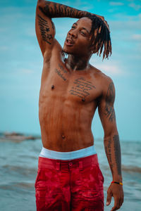 Full length of shirtless man standing at beach against sky