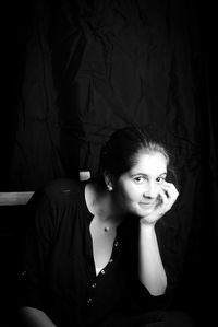 Portrait of young woman leaning on chair in darkroom