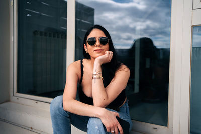 Young woman wearing sunglasses sitting by window