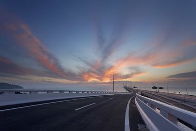 Road by sea against sky during sunset