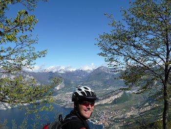 Close- up of smiling by man with helmet by lake garda and mountains against sky