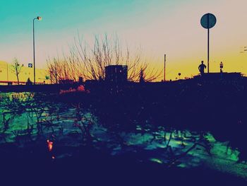 Silhouette plants by street against sky at dusk