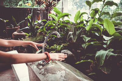 Cropped hands of girl washing hands below faucet in yard