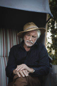 Sad senior man wearing hat sitting at farm