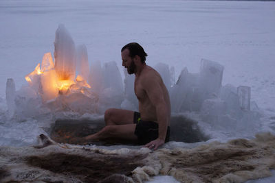 Side view of mature man taking ice bath at frozen lake during dusk