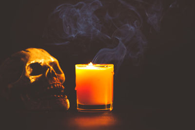 Close-up of skull by lit candle on table in darkroom