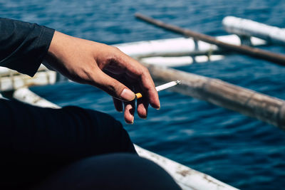 Midsection of person holding cigarette in sea