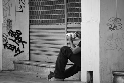 Low section of man holding food while sitting by shutter