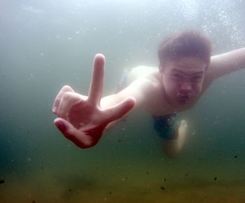 Portrait of shirtless teenage boy gesturing peace sign in sea