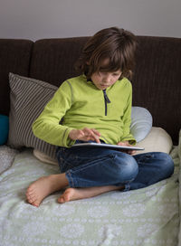 Boy using digital tablet while sitting on bed at home